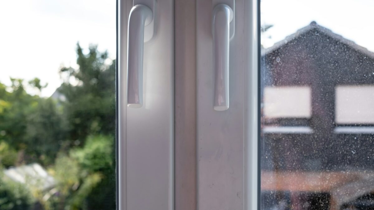 Closed white PVC window with two sashes, with dirty glass, through which the courtyard is visible