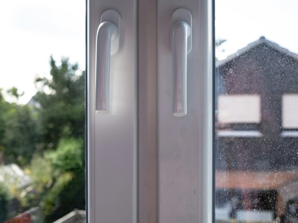 Closed white PVC window with two sashes, with dirty glass, through which the courtyard is visible